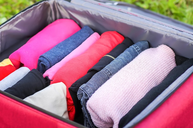 Open suitcase on the green grass with different clothes folded vertically. Vertical storage for easy travel packing.