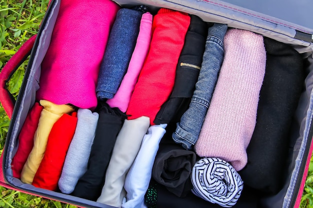 Open suitcase on the green grass with different clothes folded vertically. Vertical storage for easy travel packing.