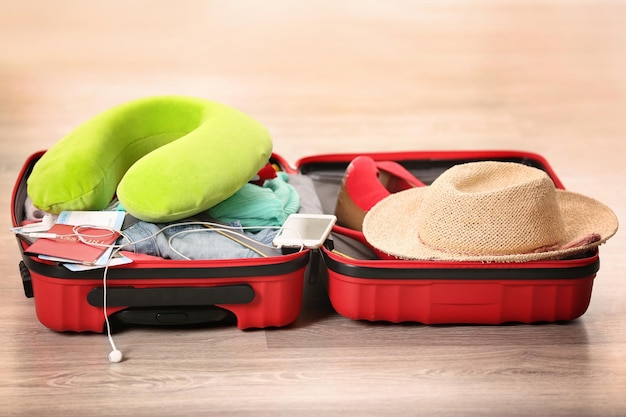 Open suitcase with different things and travel pillow on floor