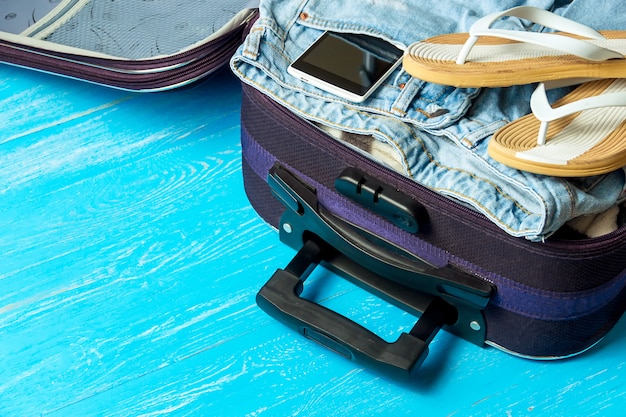 Open suitcase with travel accessories on blue wooden table 