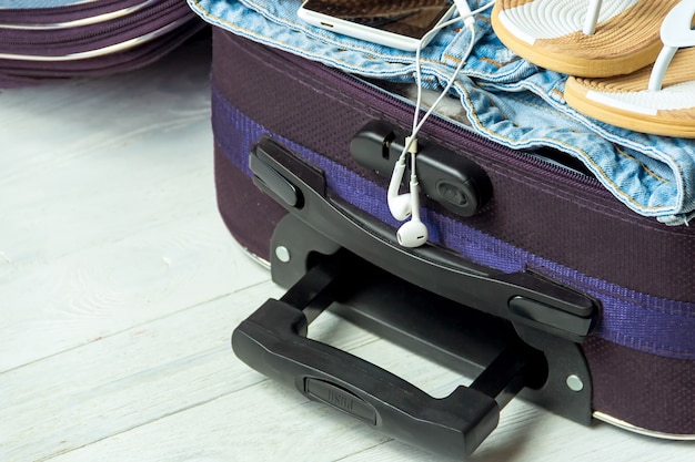 Open suitcase with travel accessories on white wooden table with copyspace.