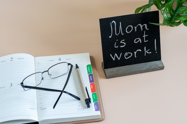 Open tijd dagboek, ogen bril en zwarte blanco met inscriptie "Mom is aan het werk". Thuis bureau.