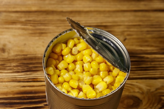 Open tin can of corn on wooden table