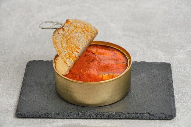 Open tin can with fish in tomato on gray concrete background