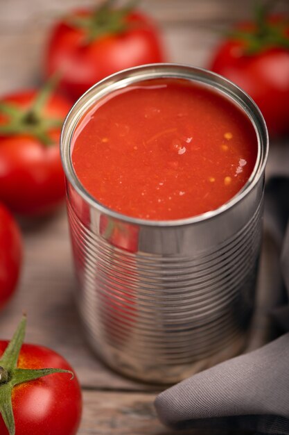 Open tin of tomatoes sauce with whole fresh tomatoes on a rustic wooden table. Close up