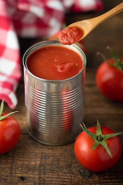 Open tin of tomatoes sauce with whole fresh tomatoes on a rustic wooden table. Close up