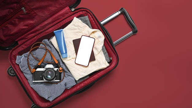 写真 服フィルムカメラスマートフォンと赤い背景のパスポートで旅行バッグを開く新しい旅のためのパッキング