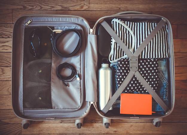 Open travel suitcase full of clothes isolated on wooden surface