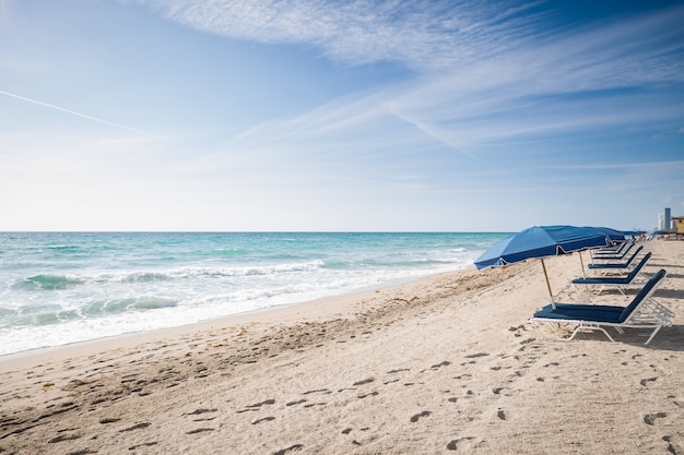 Foto ombrelloni aperti su una spiaggia sabbiosa vuota in riva all'oceano su uno sfondo di cielo blu