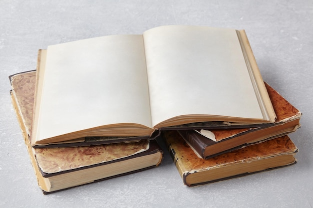 Open vintage book or notebook in a super jacket on a stack of old shabby books on a pale gray concrete table