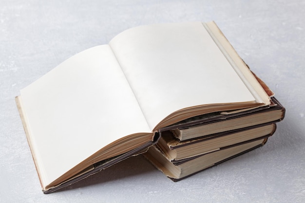 빈 페이지가 있는 열린 빈티지 책은 회색 콘크리트 테이블 Book Day Copy 공간 모형에 있는 먼지 재킷에 있는 오래된 허름한 책 더미에 놓여 있습니다.