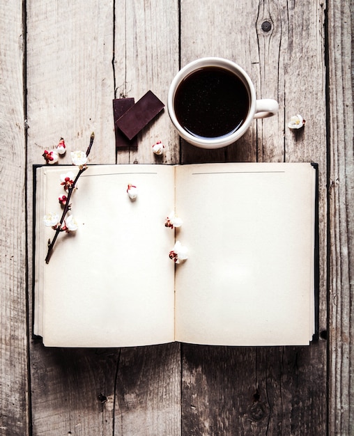 Libro aperto vintage con ramo di fiori di ciliegio, cioccolatini e tazza di caffè