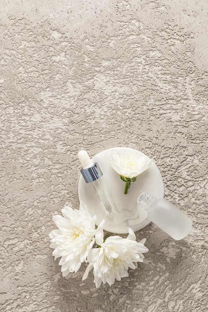 An open white matte bottle and pipette filled with cosmetics on a white round marble podium and a cement gray background A copy space