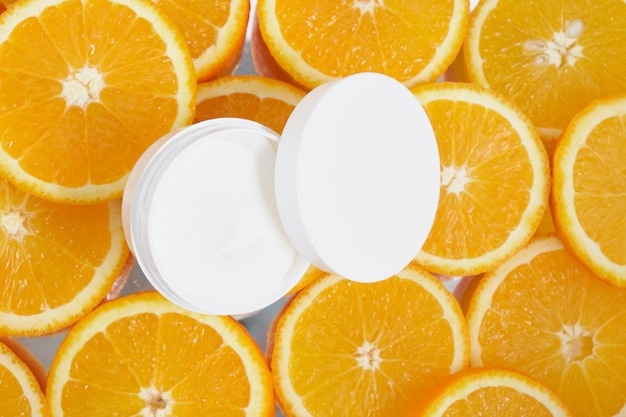 Open white plastic cream jar over sliced oranges backgronund, top view