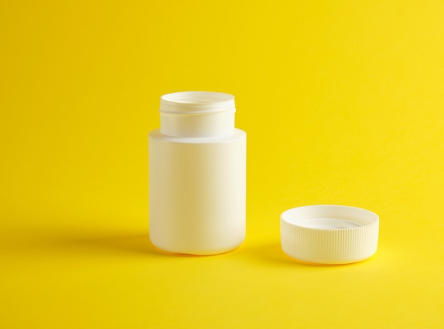 Open white plastic jar for medicines stands on a yellow 