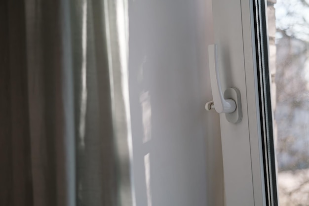 Open white PVC window with a fixing device for ventilation and a curtain under natural light