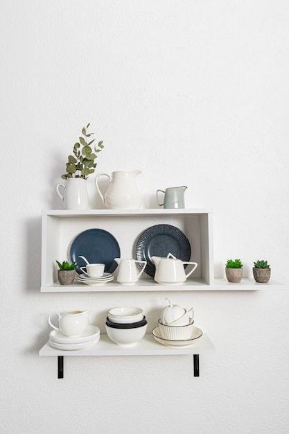 Open white wooden shelves with various dishes made of environmentally friendly materials a white textured wall Stylish design front view