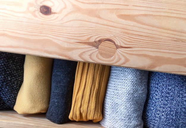 Open wooden dresser drawer with warm knitted woolen clothes Home vertical storage Wardrobe organisation Trendy colors