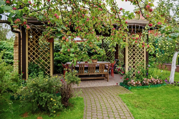 Open wooden gazebo in the garden with apple trees and flowers. Summer landscape background.