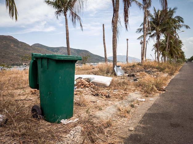 Opened big empty green plastic trash garbage bin in modern\
comfortable village near sea and palms public trash on the side of\
the road infectious control garbage disposal disposal of waste\
concept