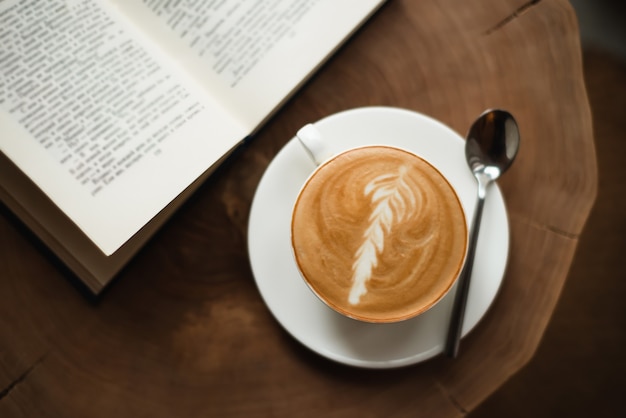 Opened book and a cup of coffee on wooden table.