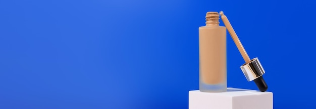 Photo opened bottle with foundation liquid beige cream on stand white podium professional makeup product