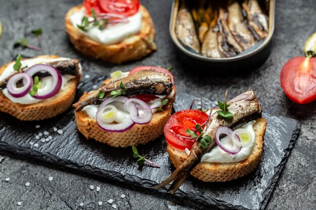 Opened cans with sprats with herbs lemon and onion Food recipe background Close up