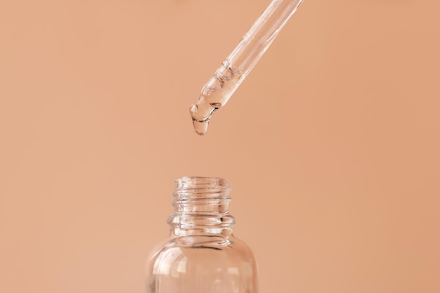 Фото Открытая косметическая бутылка с каплей сыворотки для лица, падающей с пипетки для очистки натурального масляного геля