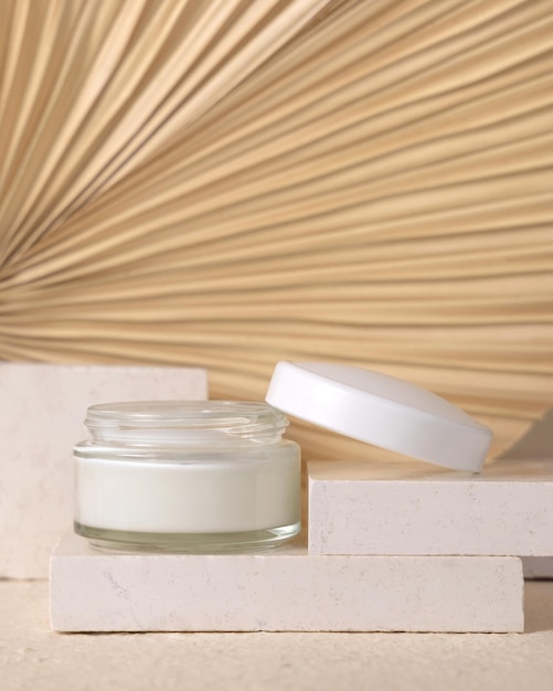 Opened cream jar on travertine stone against dry beige palm leaf close up cosmetic mockup