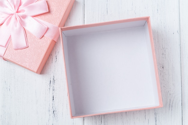 Opened empty decorative pink gift box with bow on wooden table. Mockup