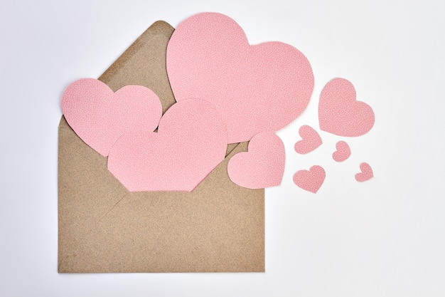 Opened envelope and pink paper hearts. Valentines Day envelope from craft paper and decorative hearts on white backgound. Express your love with letter.