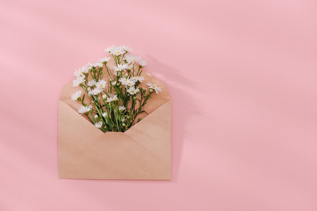 Opened envelope with flowers arrangements on pink background, top view. Festive greeting concept