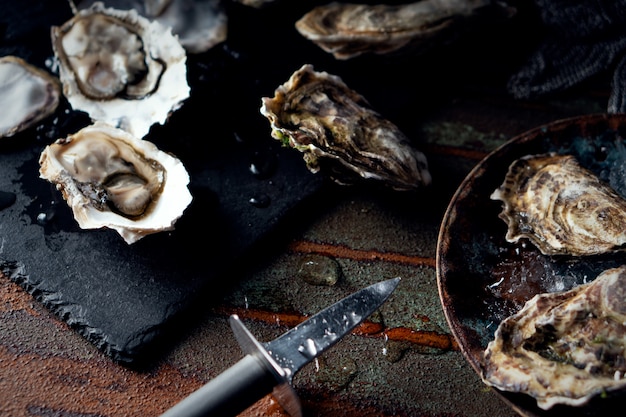 Opened fresh oysters on a dark background, a knife and water drops. Rostik style.