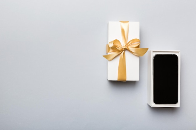 Открытая подарочная коробка с золотой лентой и смартфоном на цветном фоне, вид сверху. Пустой макет упаковки открытой коробки, шаблон для вашего дизайна - макет брендинга.