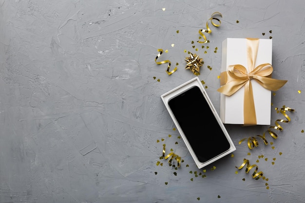 Opened gift box with gold ribbon and smartphone on color background top view Blank open box packaging mockup Template for your design branding mockup