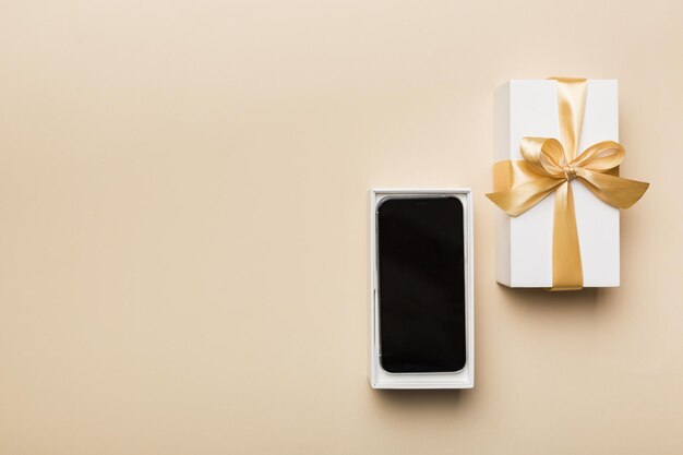 Opened gift box with gold ribbon and smartphone on color background top view Blank open box packaging mockup Template for your design branding mockup