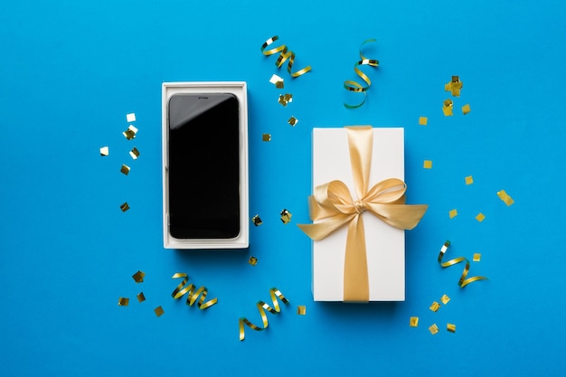 Открытая подарочная коробка с золотой лентой и смартфон на цветном фоне вид сверху Пустой макет упаковки открытой коробки Шаблон для макета вашего дизайна брендинга