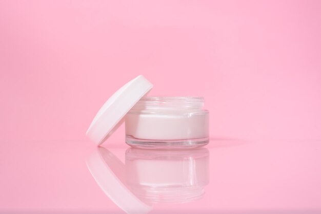 Opened jar of facial cream on the pink background