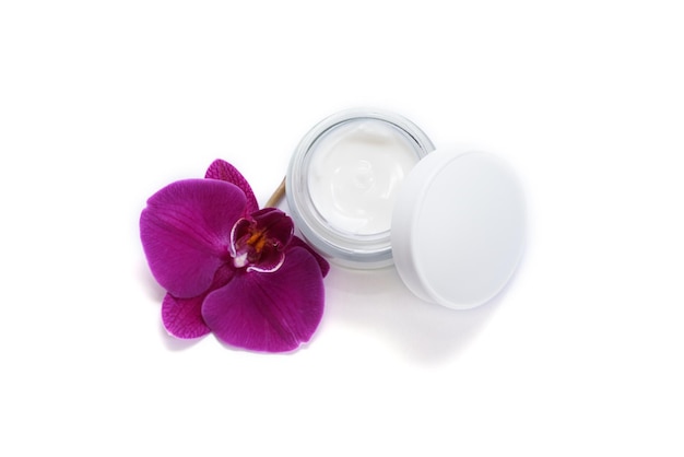 Opened jar of facial cream with many orchid flower