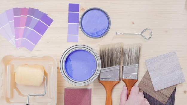 Opened metal paint can with purple paint and other paint tools on unfinished wooden background.