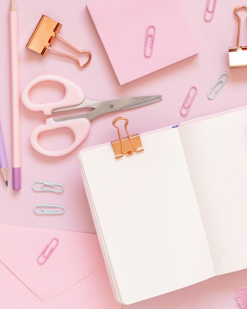 Opened notebook and Pink school accessories on pastel pink, Top view, textbook mockup. Girly workplace with scissors, pencils, paperclips, sticky note paper and envelope. Back to school concept