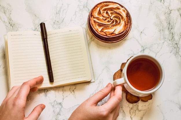 Opened notebook with blank area pen and a cup of black tea on a white marble table in morning time