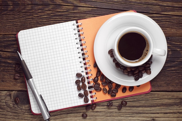 Opened notepad, pen and coffee cup on dark wooden table, top view