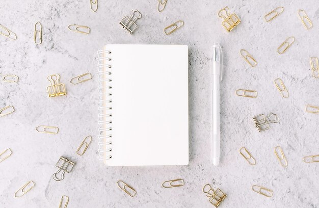 Opened notepad with white pen on background with set of silver and gold paper clips on light grey cement surface Office and business concept Flat lay