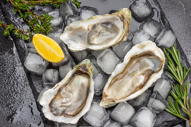 opened oyster shells with ice on black background lemon and greens on table flat lay black background