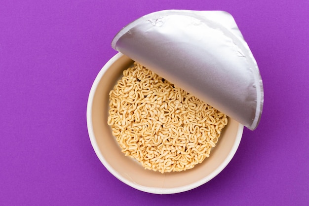 Opened package with uncooked instant noodles on violet background