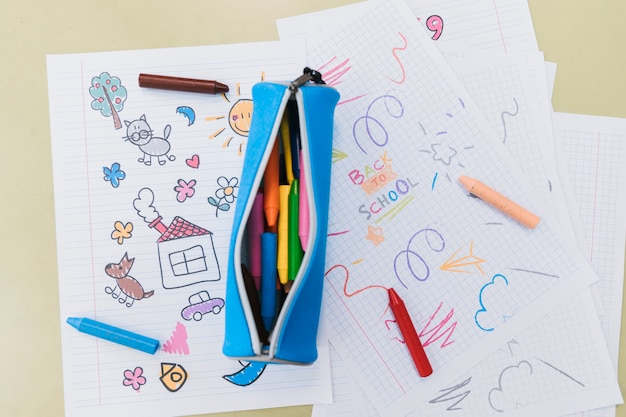 Opened pencil case and wax crayons scattered on kid drawings