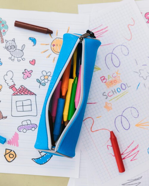 Opened pencil case with wax crayons placed kid drawings person