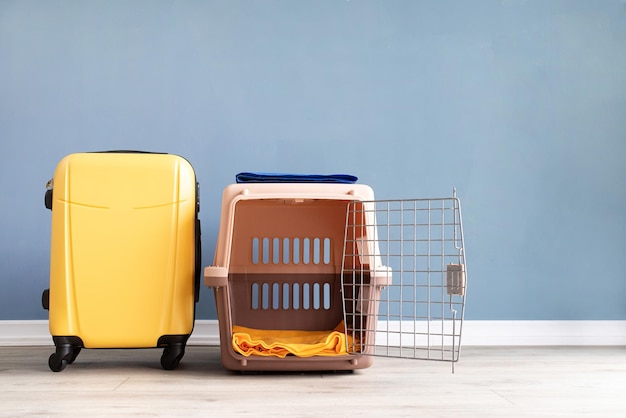 Opened plastic pet carrier or pet cage and yellow suitcase on\
the floor at home copy space