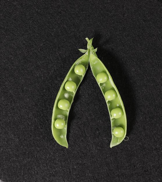 Opened pod of green peas with seeds on a black background